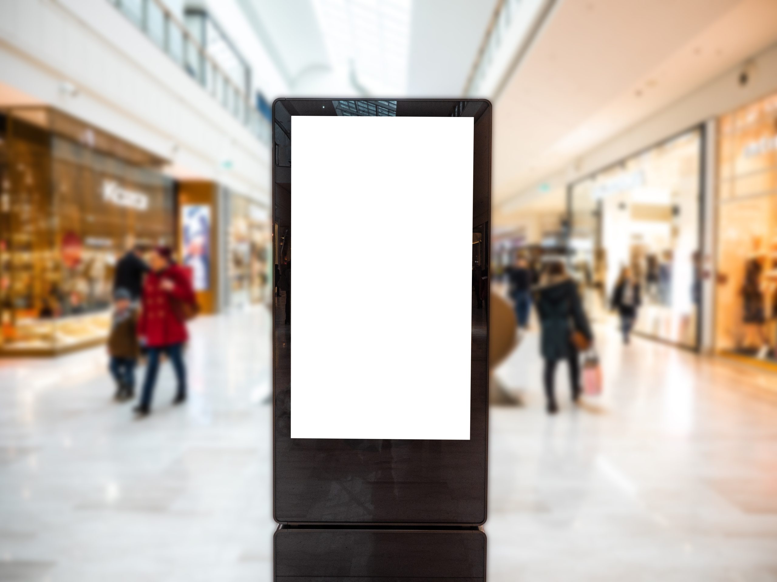 A digital billboard with a blank white screen stands prominently in the shopping mall, seamlessly blending into the bustling scene of blurred shoppers and vibrant storefronts, serving as an ideal canvas for innovative digital signage.
