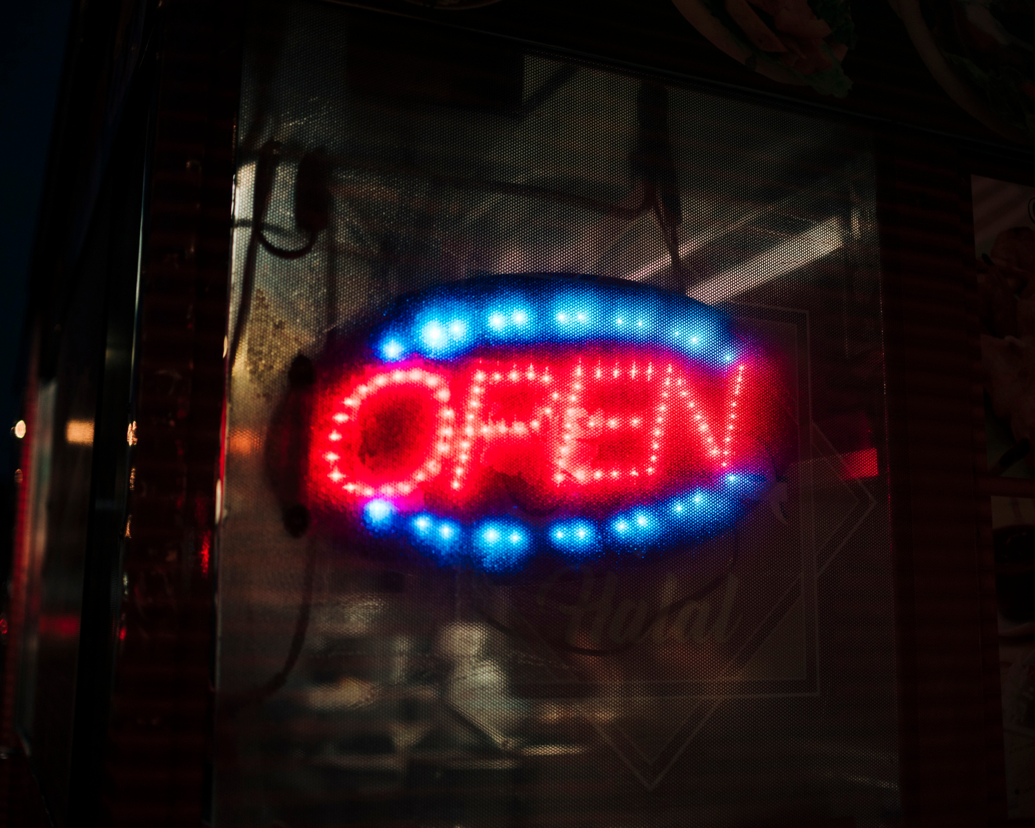 A neon "OPEN" sign with red and blue lights is glowing in a dark window.