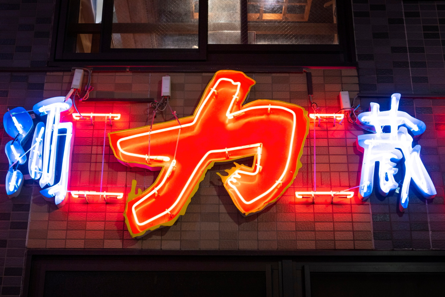 2149836918 Neon Japanese sign with large red and yellow central character, flanked by blue characters on each side.